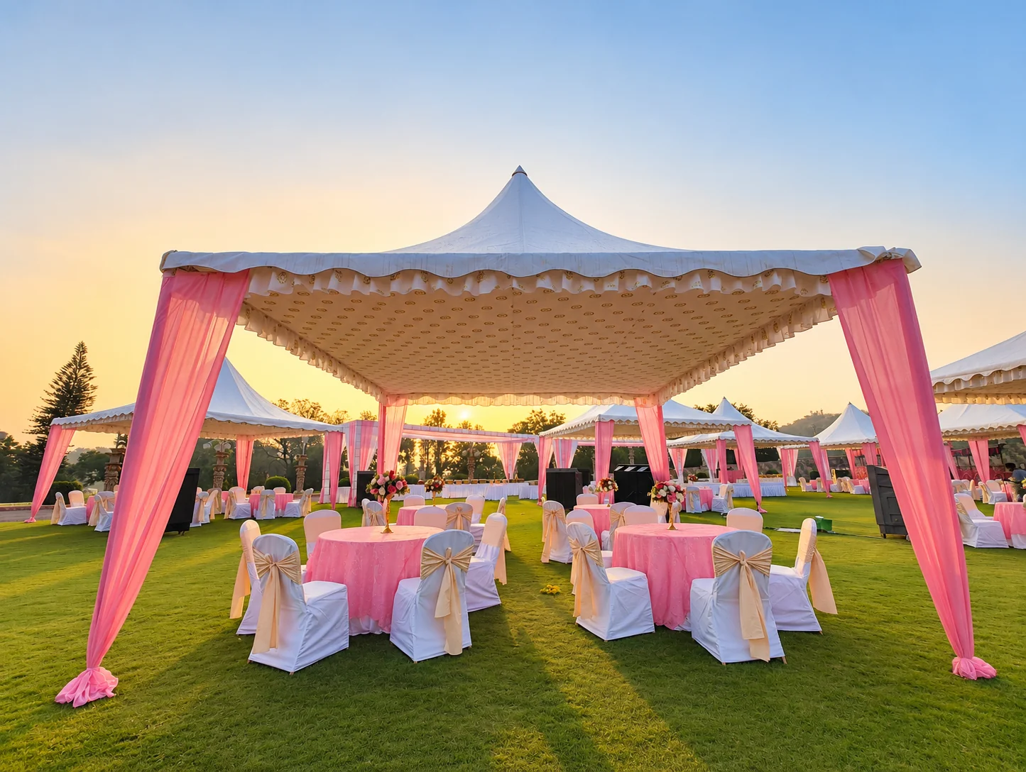 Pink gazebo drapes and round dining tables on a lawn at sunrise