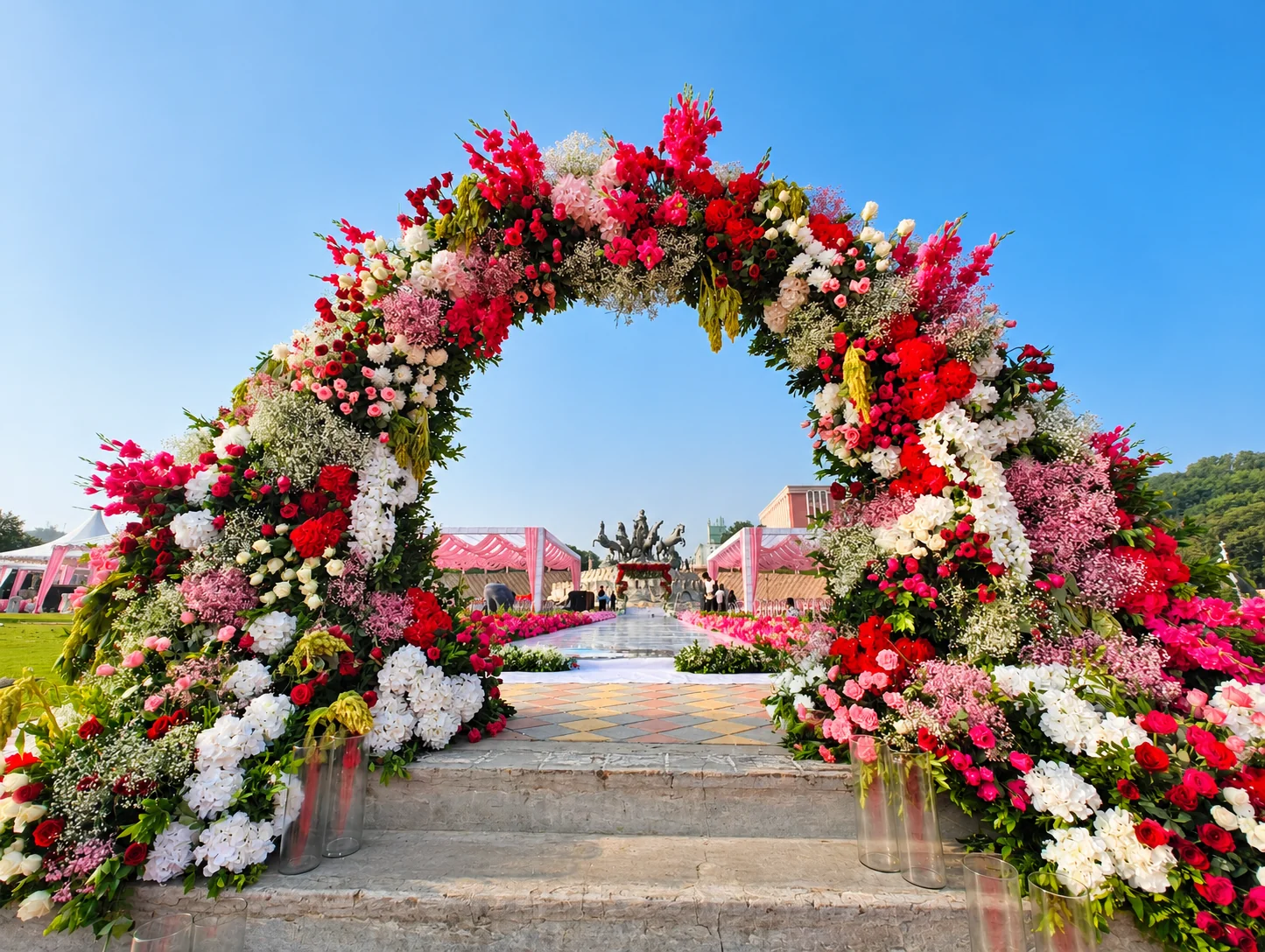 Pink, red and white floral entrance arch overlooking pink event canopies