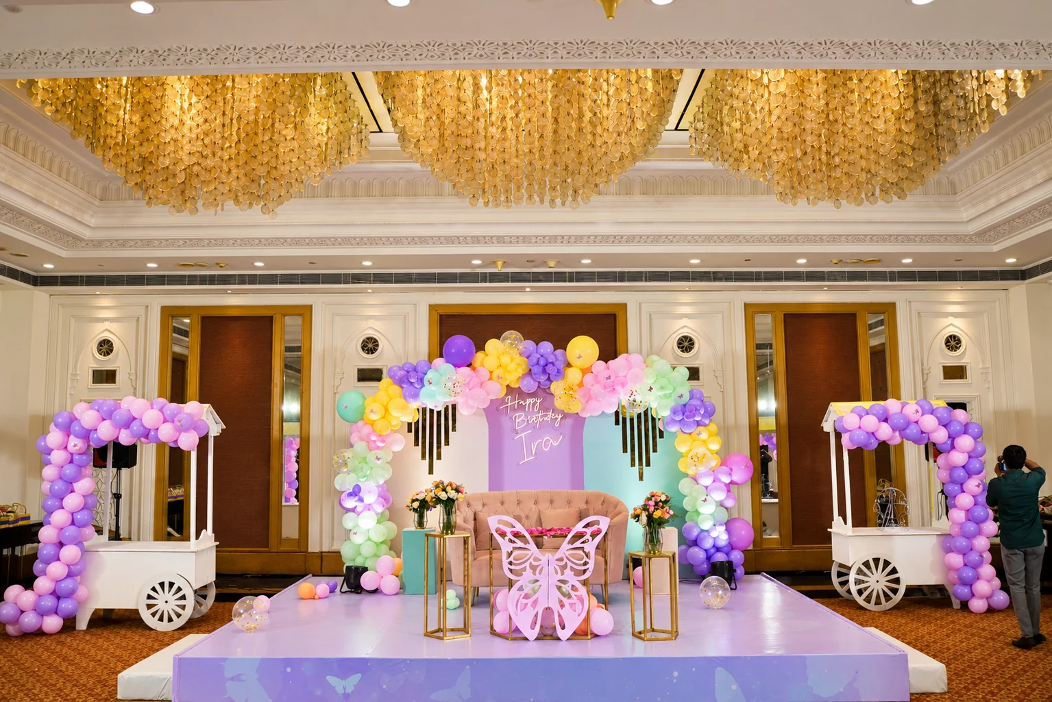 Pastel balloon birthday stage with butterfly details and white carts