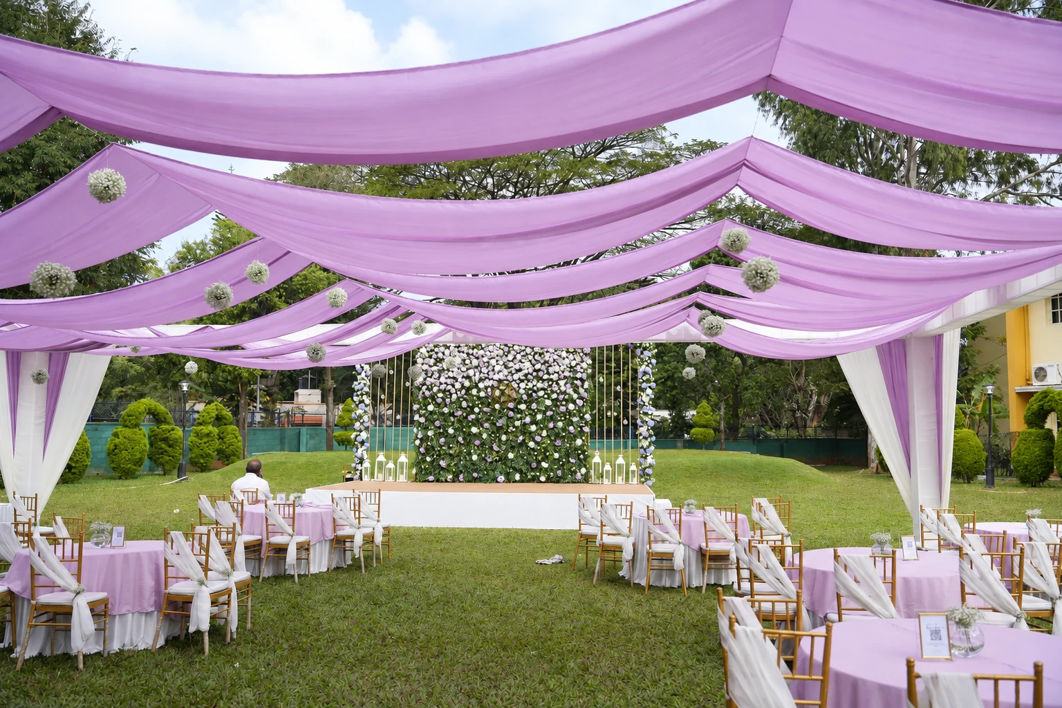 Lilac draped garden canopy with white flowers and a floral engagement backdrop